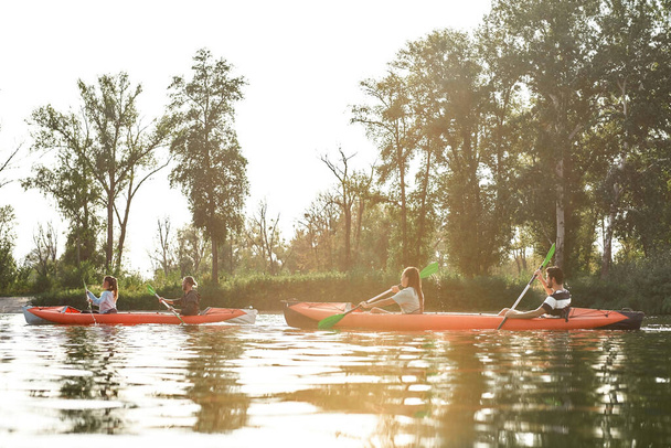 Canoe with active young friends paddling together on a river surrounded by peaceful summer nature on a weekend - Fotoğraf, Görsel