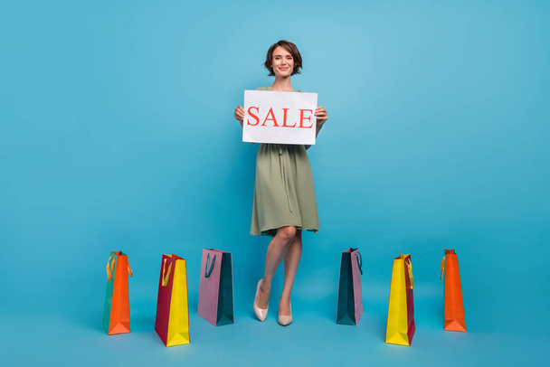Full body photo of positive cheerful young woman hand banner sale bags buy isolated on blue color background - Fotografie, Obrázek