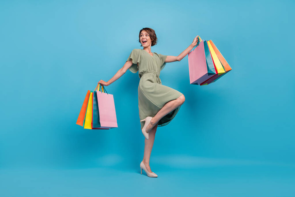 Full body photo of positive dreamy happy young woman hand shopping bags look empty space isolated on blue color background - Foto, immagini