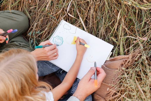 Ένα κοριτσάκι ζωγραφίζει με τους γονείς της σε ένα πικνίκ. κοντινό πλάνο - Φωτογραφία, εικόνα