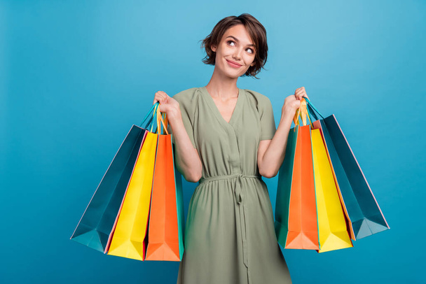 Photo of cheerful dreamy young woman hold hands shopping bag look empty space isolated on blue color background - Fotoğraf, Görsel