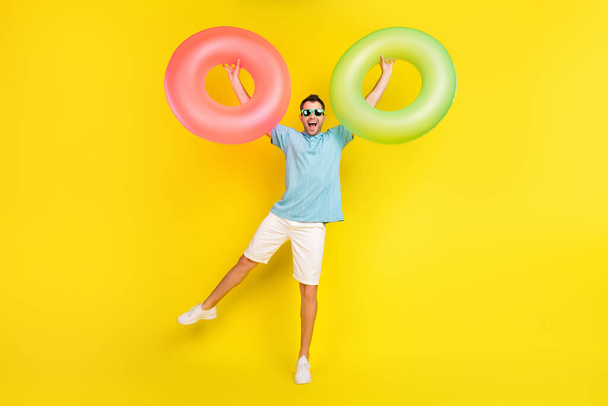 Photo of charming funny young man wear blue t-shirt dark glasses rising water circles smiling isolated yellow color background - Фото, зображення