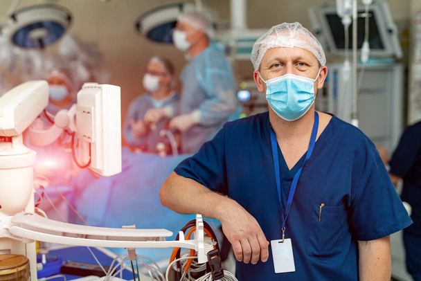 Portrait of male surgeon in operation theater looking at camera. Doctor in scrubs and medical mask in modern hospital operating room - Фото, зображення