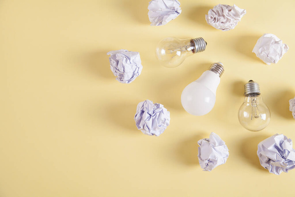 Creativity inspiration. Light bulbs and crumpled paper balls on yellow background. - Photo, image