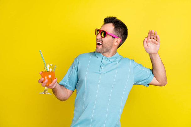 Photo of funny brunet man hold cocktail look empty space wear eyewear blue t-shirt isolated on yellow color background - Fotó, kép