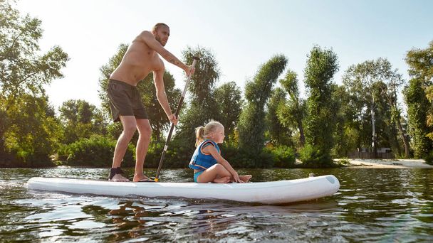 夏の日に美しい自然に囲まれた川でサーフィンをして、彼の娘と一緒にリラックスしてください。 - 写真・画像