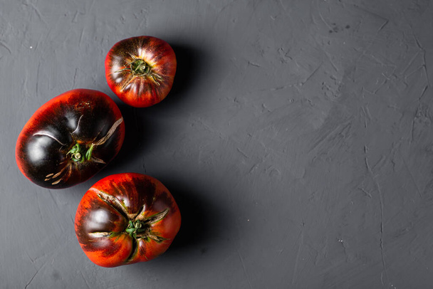 Red-black tomatoes of the bovine heart variety on a black background. - Zdjęcie, obraz