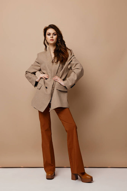 sexy woman in coat pants and boots posing on a beige background - Photo, Image