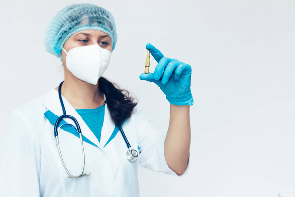Een medische vrouw houdt een ampul met een vaccin of medicijn in haar hand en kijkt ernaar. Een nieuw vaccin voor covid 19. - Foto, afbeelding