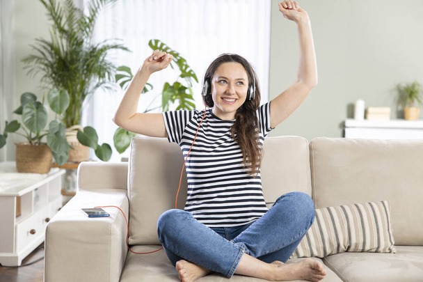 Young woman wearing headphones dancing in living room at hom - Photo, Image