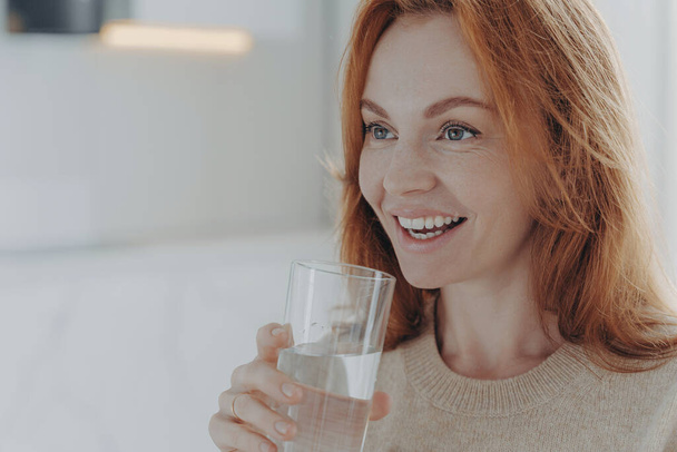 Ginger woman drinks pure water from glass enjoys refreshing drink - Photo, Image