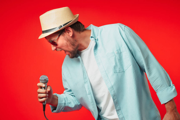 Portrét muže středního věku v klobouku drží v ruce mikrofon a emocionálně zpívá píseň. - Fotografie, Obrázek