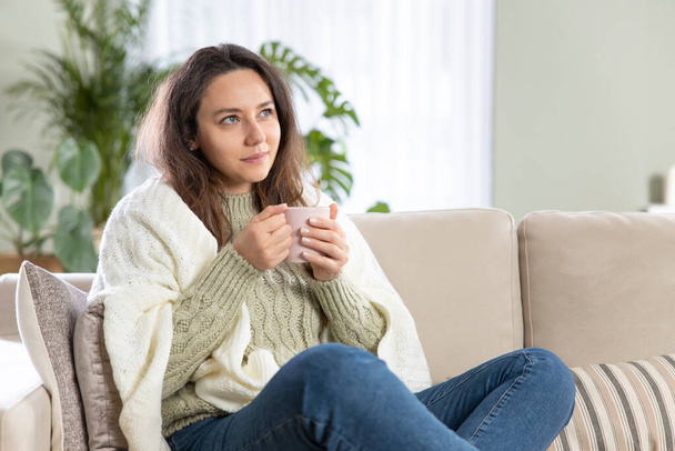Young woman sit down on the sofa drinking coffee. Leisure activity, lifestyle for people concept. - Photo, image