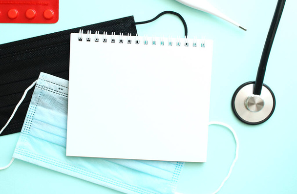 Cuaderno que se encuentra sobre un fondo azul junto a una máscara médica - Foto, Imagen