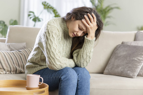 Fiatal depressziós nő ül a kanapén a nappaliban. Szomorú és aggódó depresszióban szenved a mentális egészségben. Problémák és összetört szív koncepció. - Fotó, kép