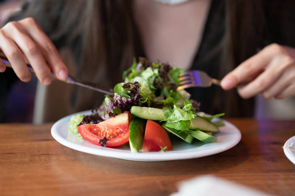 Millennial male no face having vegetables, healthy eating and lifestyle concept. Unrecognizable man eat organic food in office. Hand hold fork with tomatoes. Adult has lunch with fresh greek salad. High quality photo - Photo, Image