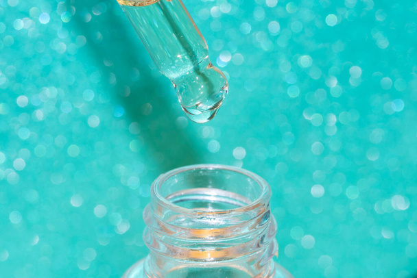 Yüzü serumla kaplı pipette damlatıcısının ayrıntıları turkuaz yeşil parlak arka planda bir şişe ile - Fotoğraf, Görsel