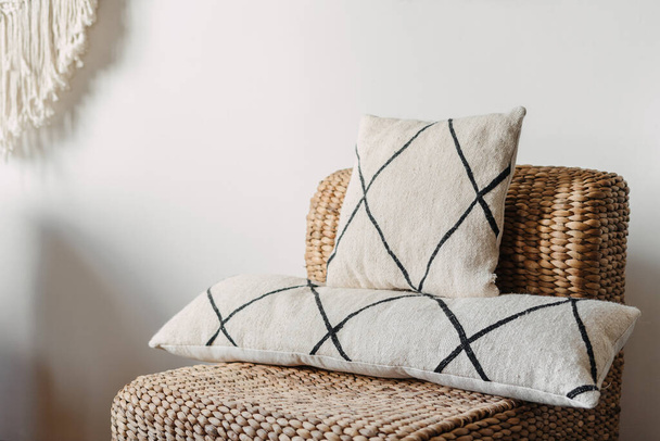 Close up view on soft cushions on comfortable wicker armchair in hygge house. Living room with ethnic boho interior, home decor and rattan furniture against white copy space wall - Fotó, kép
