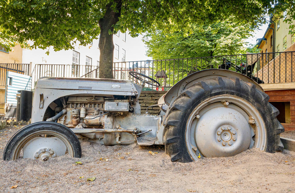 Estocolmo, Suecia - 19 de junio: Un viejo tractor oxidado con ruedas en la arena como parte de un parque infantil en el jardín de infancia de Estocolmo - Foto, imagen