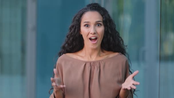 Geschokt verrast latino meisje dolblij mooi brunette millennial vrouw cover mond met shock winnaar gebaar oprechte gelukkig vreugde emoties verbazing geïsoleerd op stad gebouw achtergrond - Video