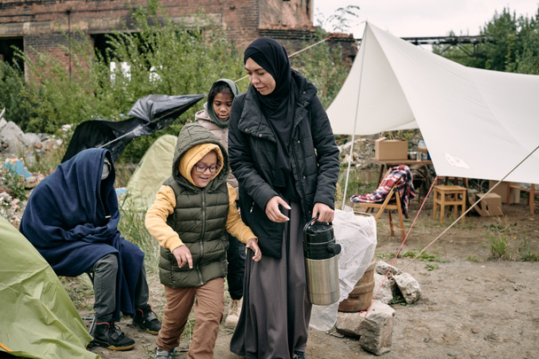 Mutter trägt Thermoskanne durch Flüchtlingslager - Foto, Bild
