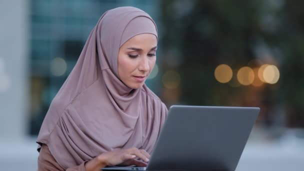 Retrato de la joven musulmana usuaria mujer de negocios estudiante chica islámica en hijab se sienta en la calle mirando en el ordenador portátil se siente sorpresa lee buenas noticias en línea en obras de Internet de forma remota recibe una oferta de correo electrónico - Metraje, vídeo