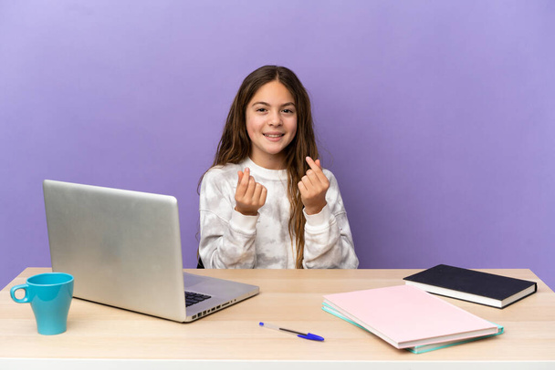Petite étudiante dans un lieu de travail avec un ordinateur portable isolé sur fond violet faisant geste d'argent - Photo, image