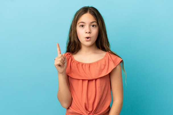 Klein blank meisje geïsoleerd op blauwe achtergrond van plan om de oplossing te realiseren terwijl het optillen van een vinger omhoog - Foto, afbeelding