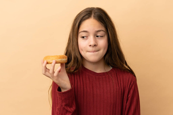 Little caucasian girl isolated on beige background holding a donut - Photo, Image