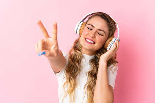 Junge Brasilianerin isoliert auf rosa Hintergrund Musik hören und singen - Foto, Bild