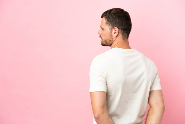 Young Brazilian man isolated on pink background in back position and looking back - Photo, Image
