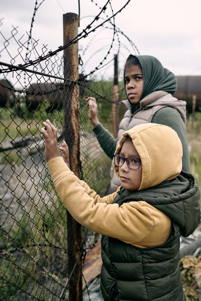 Потерянные дети стоят у колючей проволоки - Фото, изображение