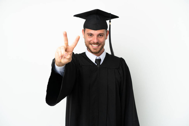 Young university Brazilian graduate isolated on white background smiling and showing victory sign - 写真・画像