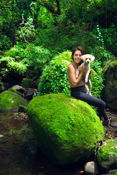 Jonge vrouw poseert met haar puppy in het tropisch bos. Vrouw en huisdier in groen nat bos op zonnige dag. Duurzaam toerisme. Amatlan, Mexico. - Foto, afbeelding