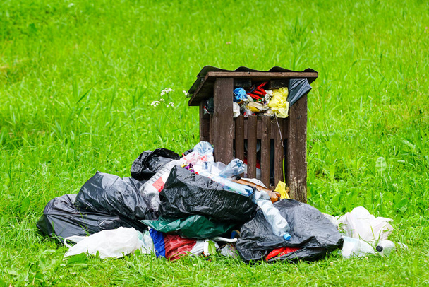 cubo de basura con basura desbordante en un prado verde - Foto, Imagen