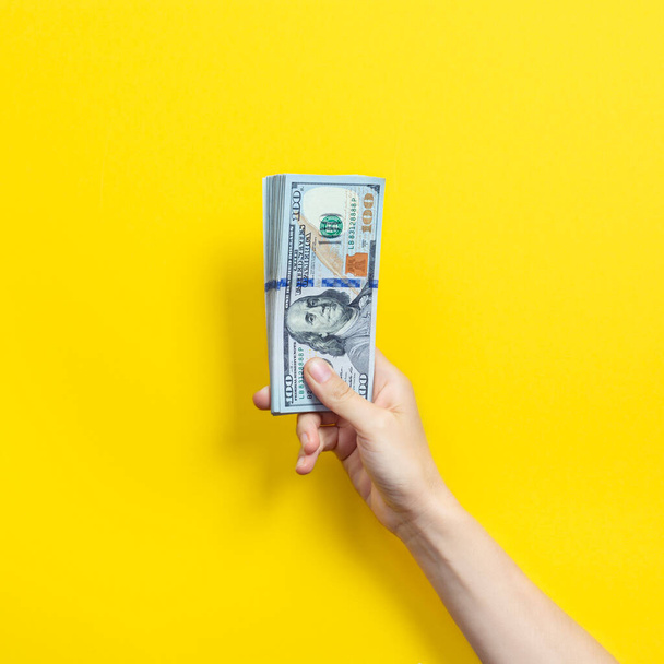 Hand holding a big stack of banknotes isolated on yellow background. Wealth or loan concept - Фото, зображення