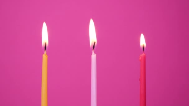 Zdmuchanie trzech świeczek na różowym tle. Zbliżenie na cios z żółtych, różowych i magenta świec ciasto. Full HD rozdzielczość slow motion szczęśliwy urodziny wideo - Materiał filmowy, wideo