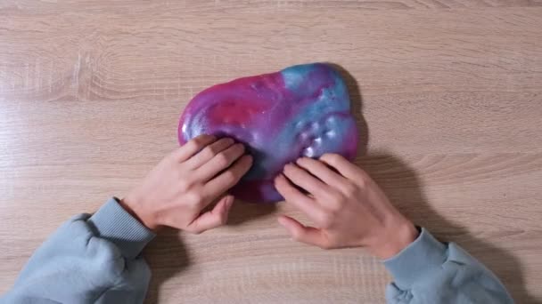 Playing with slime, stretching the gooey substance for fun and stress relief. Close up and top view of female hand holding blue, pink and purple shining slime and squeezing it. 4K video - Footage, Video