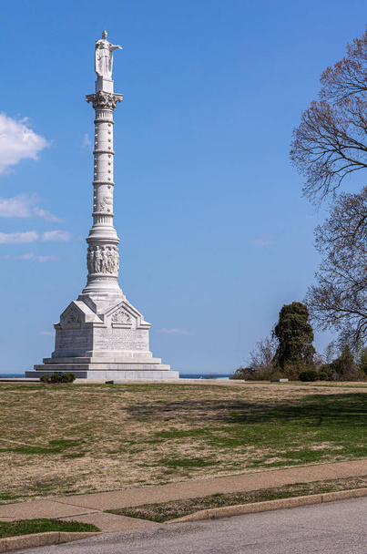 USA, Virginia, Yorktown - 30 maart 2013: Yorktown Victory Monument, compleet witstenen monument met standbeelden tegen de blauwe hemel, staat op groen-bruine heuvel. - Foto, afbeelding