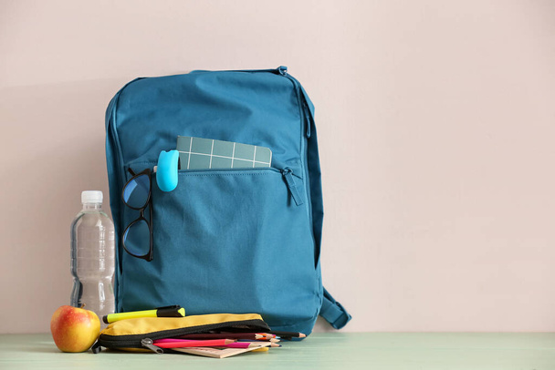 Стильний шкільний рюкзак з канцтоварами, окулярами, пляшкою води та яблуком на столі
 - Фото, зображення