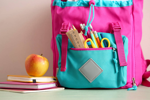 Schulrucksack mit Schreibwaren und Apfel auf dem Tisch, Nahaufnahme - Foto, Bild