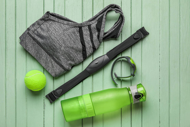フィットネストラッカー、胸ベルト、テニスボール、水のボトルと色の木製の背景にスポーツトップ - 写真・画像