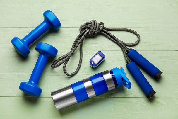 Pulse oximeter, bottle of water and sport equipment on color wooden background - Φωτογραφία, εικόνα