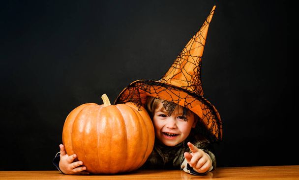 Joyeux Halloween. Petit garçon au chapeau de sorcière avec la citrouille d'Halloween pointant vers toi. Trucs ou friandises. Enfant avec Jack-o-lantern. - Photo, image