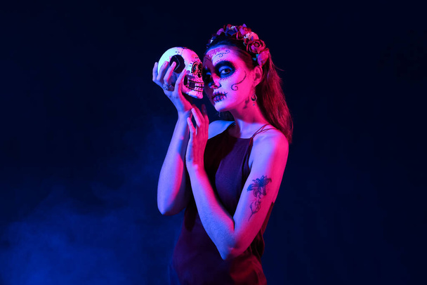 Молода жінка з намальованим обличчям і цукром для Мексиканського Дня Мертвих (El Dia de Muertos) на темному тлі - Фото, зображення