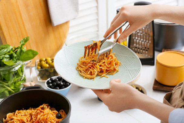 Woman preparing tasty Pasta Puttanesca at kitchen table - Фото, изображение