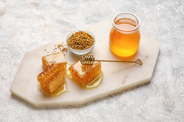 Jar of honey, combs and bee pollen on light background - Фото, изображение