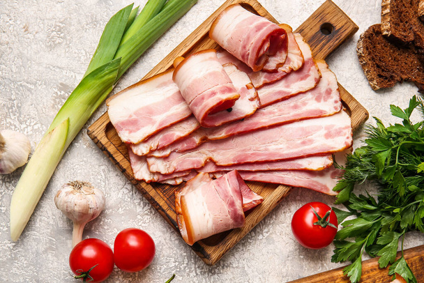 Wooden board with slices of tasty smoked bacon and fresh vegetables on light background - Photo, image