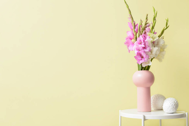 Βάζο με όμορφα λουλούδια γλαδιόλα και διακόσμηση στο τραπέζι κοντά στον τοίχο χρώμα - Φωτογραφία, εικόνα