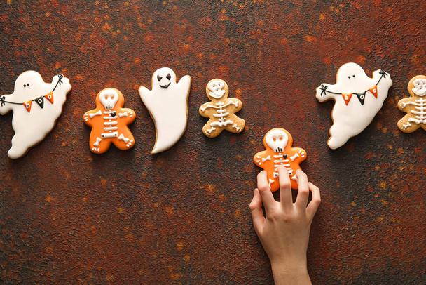 Female hand with tasty cookies for Halloween celebration on color background - 写真・画像